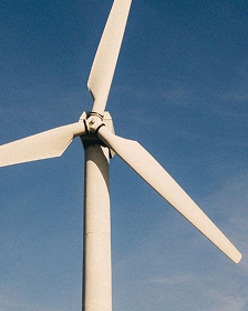 Photograph of a wind turbine rotor and hub against blue sky, representing wind power and renewable energy infrastructure.