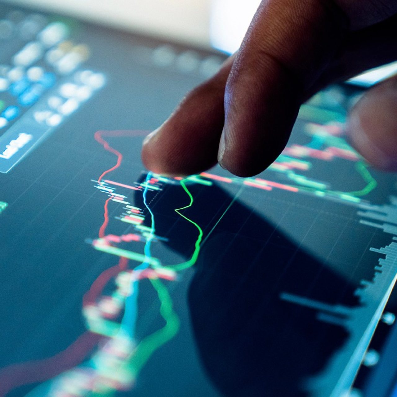 Photo of a hand on a tablet showing financial market charts with candlesticks and trend lines, conveying data analysis.